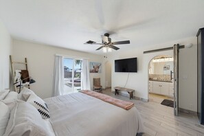 A bedroom with a bed, a ceiling fan, a TV, a window with curtains, and a door leading to a bathroom. - Tranquil Lake Havasu Getaway - Private Pool - Rooftop Patio (Lake Havasu City)