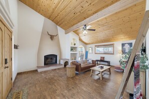 A spacious living area with a fireplace, wooden flooring, a ceiling fan, and a large window. - Tranquil Lake Havasu Getaway - Private Pool - Rooftop Patio (Lake Havasu City)