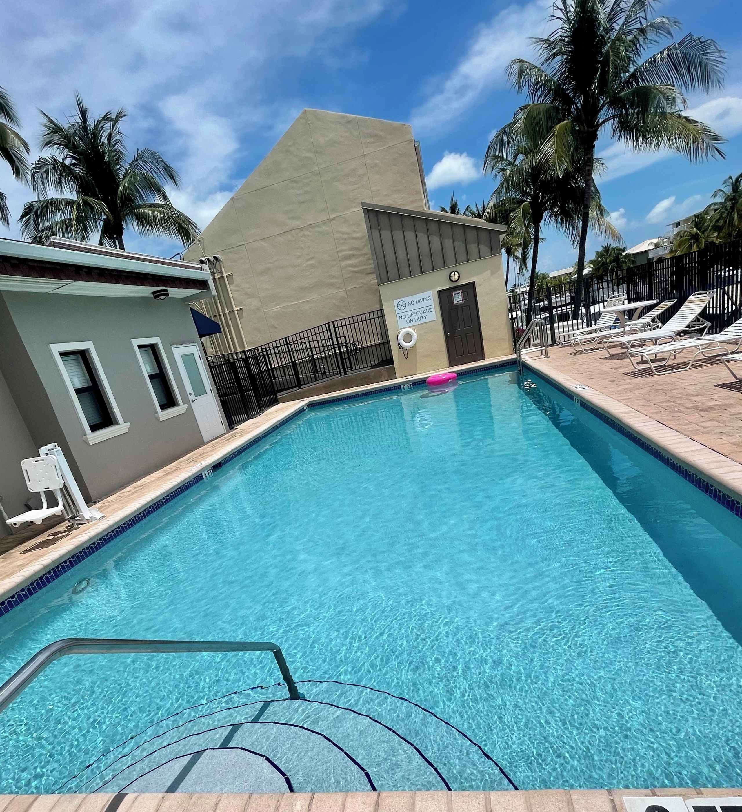 Una piscina con socorrista, sillas de descanso y palmeras.