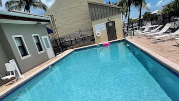 Una piscina con socorrista, sillas de descanso y palmeras.