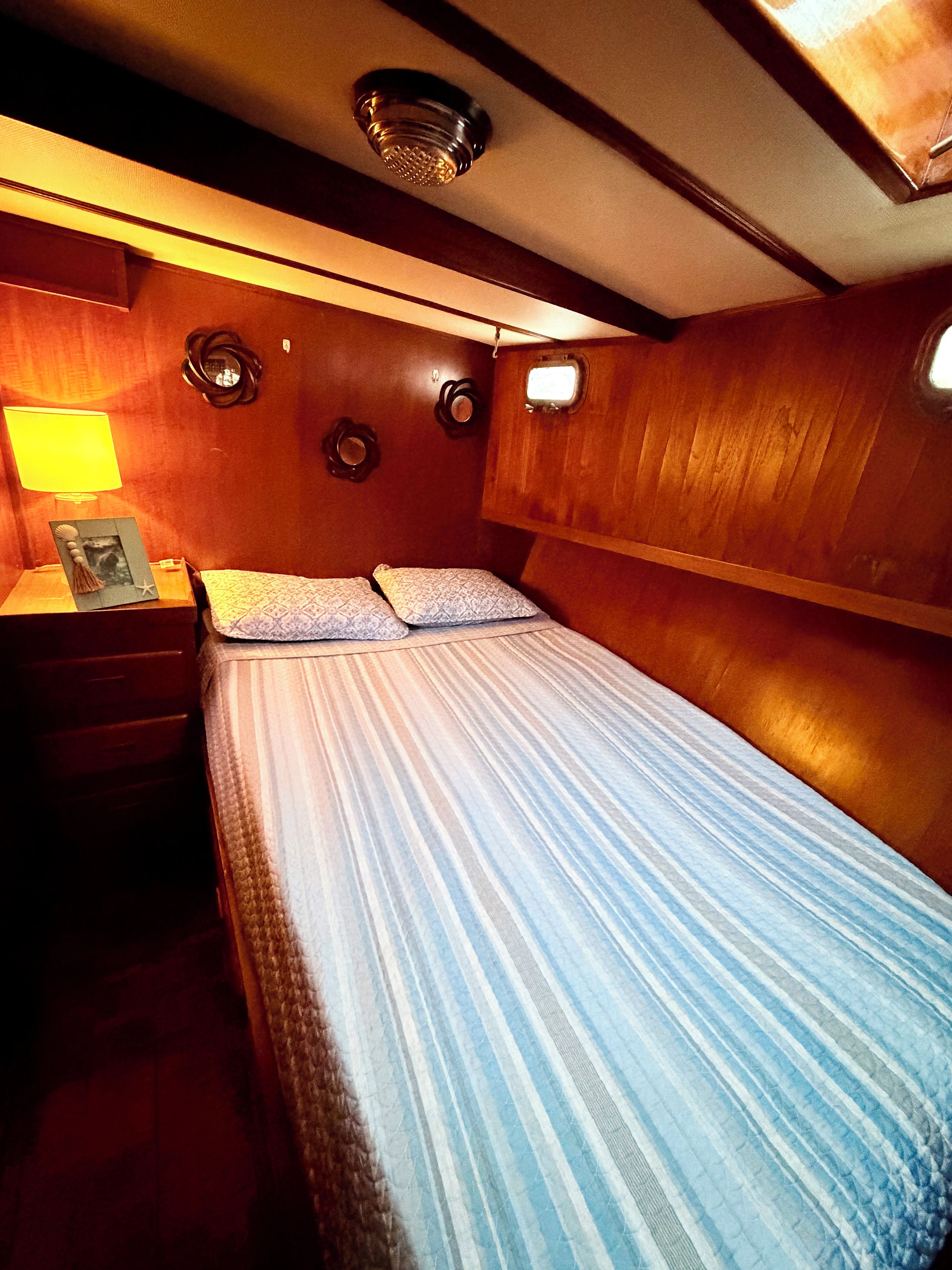 Une cabine comprenant un lit, une table de chevet, une lampe et une petite fenêtre.