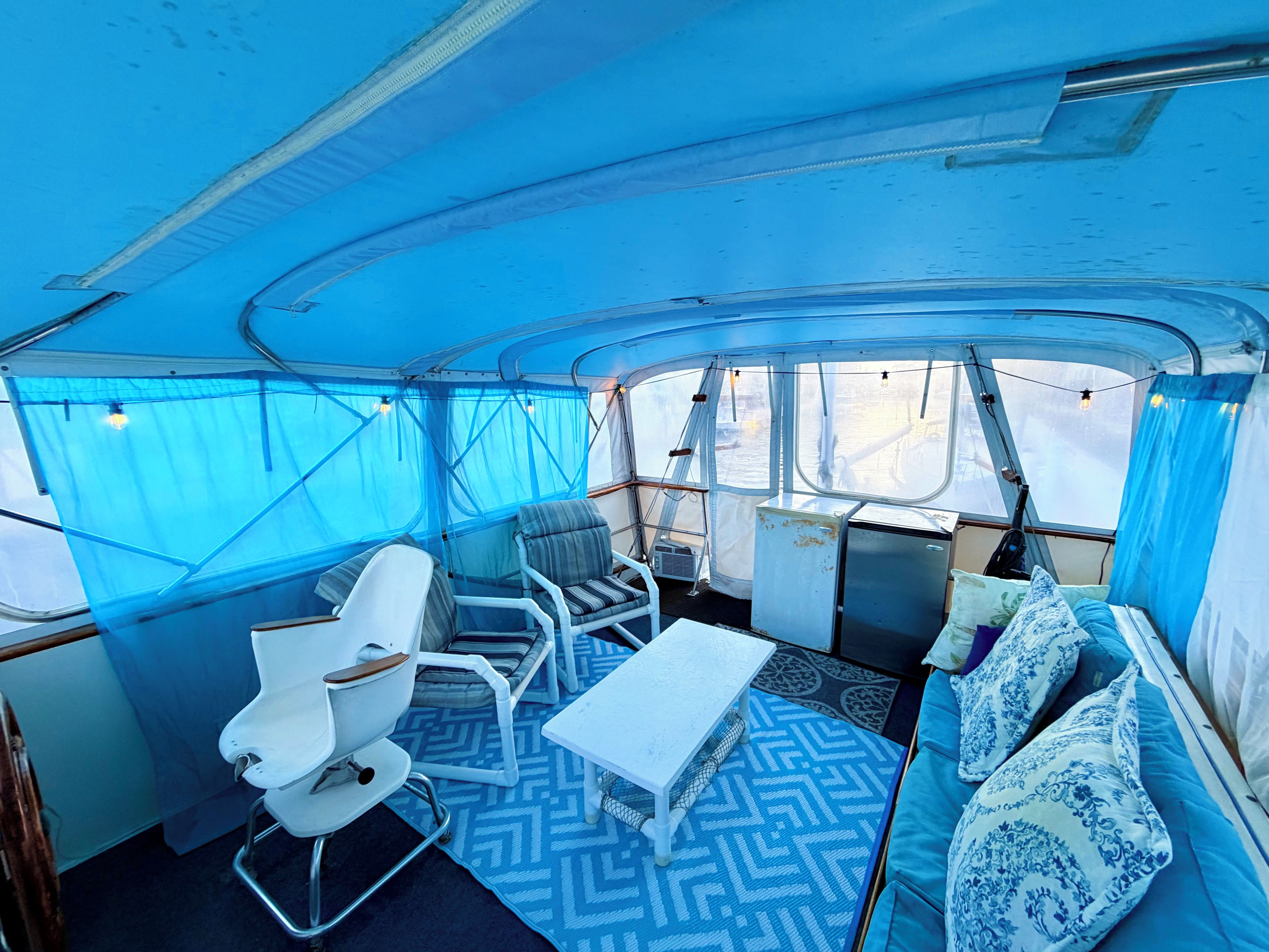 L'intérieur d'un bateau avec une table blanche, deux chaises, un canapé et un tapis à motifs.