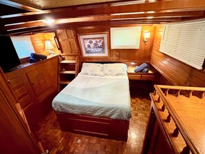 Une chambre à coucher bien éclairée et de taille modeste, comprenant un lit, un bureau et une chaise. On y trouve une fenêtre avec des stores, un tableau encadré au mur et un plancher en bois.