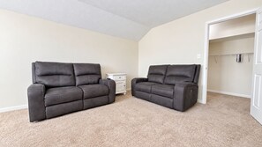 A room with beige carpet, two dark-colored sofas, a white dresser, and a closet with hanging clothes. - The Happy Habitat (Clarksville)