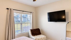 A bedroom with a bed, a chair, a television on the wall, and a window with blinds. - The Happy Habitat (Clarksville)