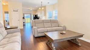 A spacious living area with a sofa set, a wooden coffee table, and a view of the kitchen and backyard. - The Happy Habitat (Clarksville)
