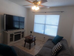 A living room with a television, a ceiling fan, a window with blinds, a small table, and a sofa with a pillow. - Cozy San Riveria Pool property near Sea World 3bed 2bath house with fireplace! (San Antonio)