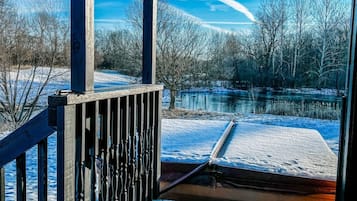 Une terrasse en bois avec une rambarde en métal, donnant sur un paysage enneigé avec une étendue d’eau et des arbres.