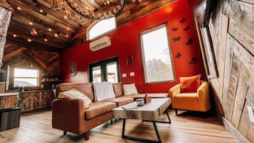L'intérieur d'un chalet accueillant, avec un plafond en bois, un mur rouge, un canapé, une table basse et un petit fauteuil orange.