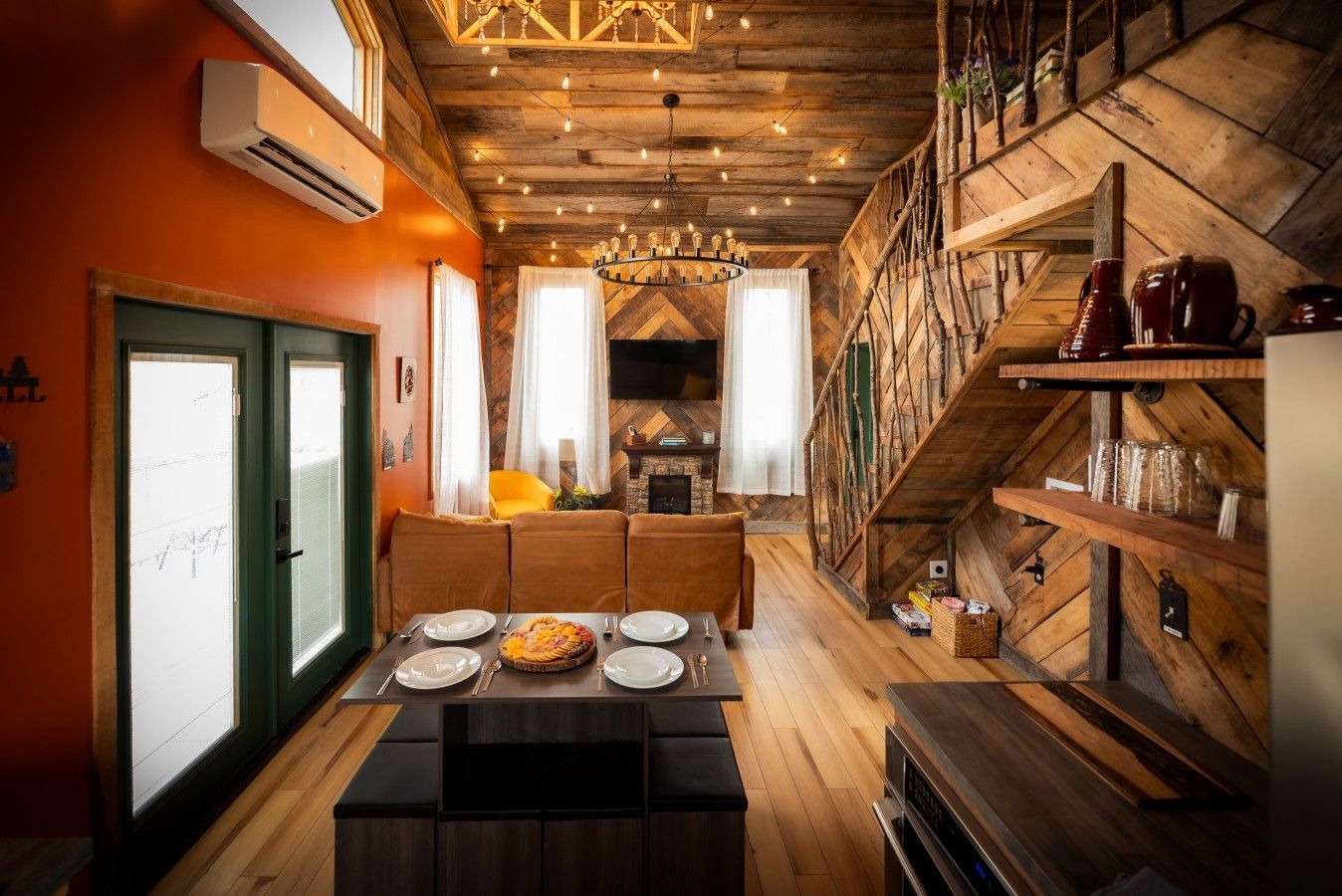 A cozy dining area with a wooden table set for four, a fireplace, and a staircase with rustic decor.