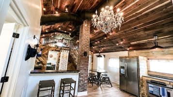 Une cuisine rustique avec un plafond en bois, un lustre, un réfrigérateur et un coin repas équipé de tabourets.