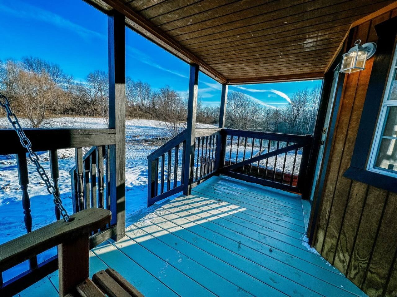Une terrasse en bois avec une rambarde, une lanterne et une vue sur un paysage enneigé.