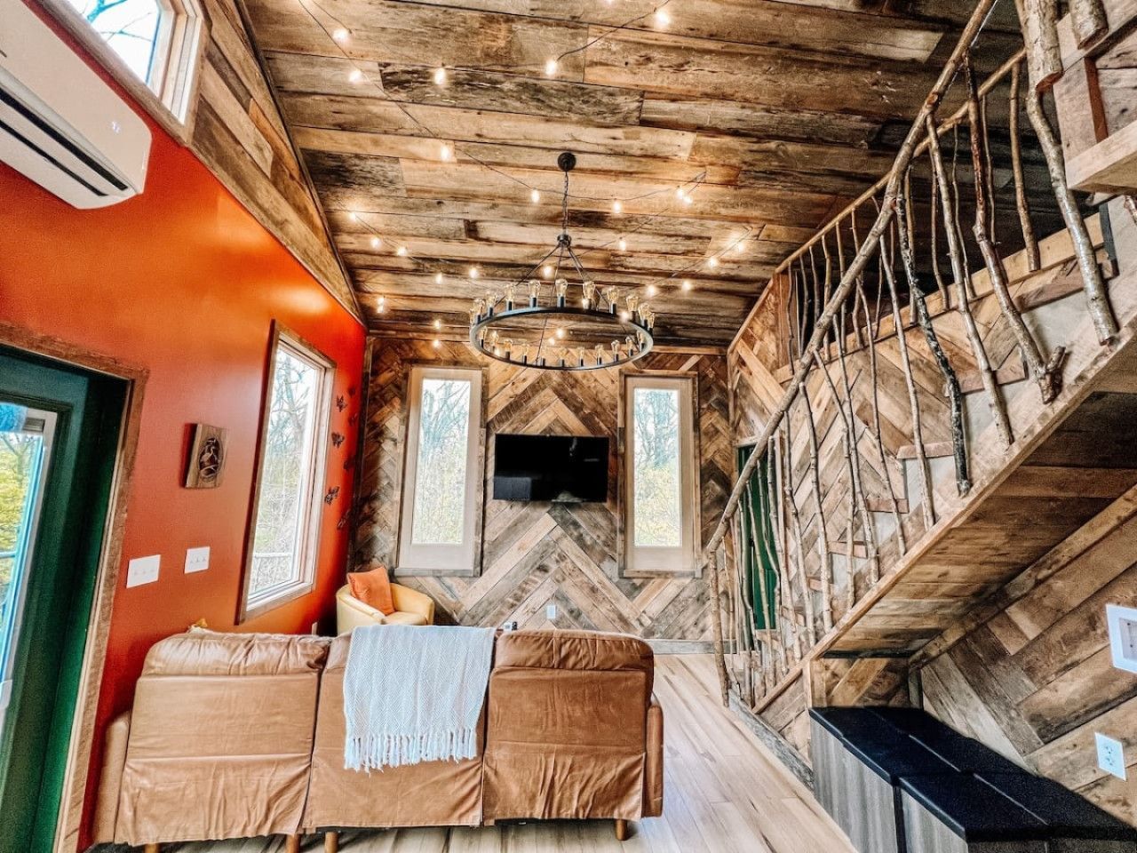 A cabin interior with a wooden ceiling, a sofa, a television, and a staircase.