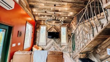 A cabin interior with a wooden ceiling, a sofa, a television, and a staircase.