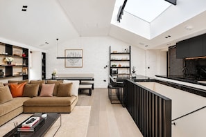 A modern interior with a living area, kitchen, and dining space, featuring a high ceiling and skylight. - Mayfair Duplex Private Terrace AC (London)