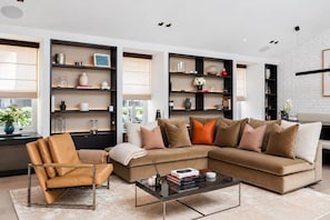 A modern living room with a sectional sofa, a leather armchair, and built-in shelving with decorative items. - Mayfair Duplex Private Terrace AC (London)