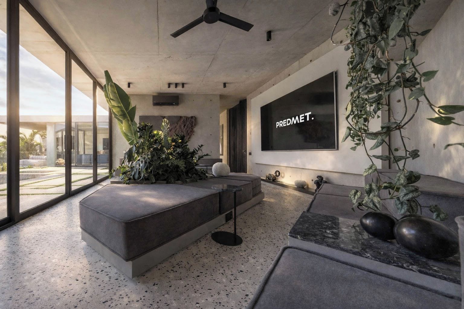 Ein modernes Wohnzimmer mit einem großen Fenster, einem grauen Sofa, einem Couchtisch und einem an der Wand befestigten Fernseher, der 'PREDMET I' anzeigt.
