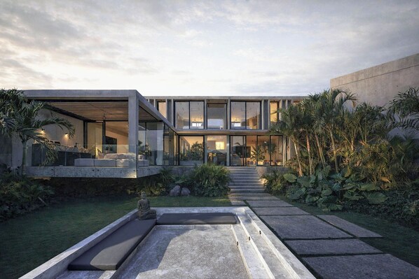 Una casa moderna con fachada de vidrio, mobiliario exterior y un jardín cuidado.