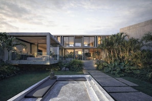 Una casa moderna con fachada de vidrio, mobiliario exterior y un jardín cuidado.