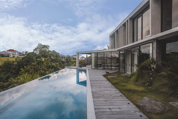 Una casa moderna con fachada de vidrio, terraza de madera y piscina.