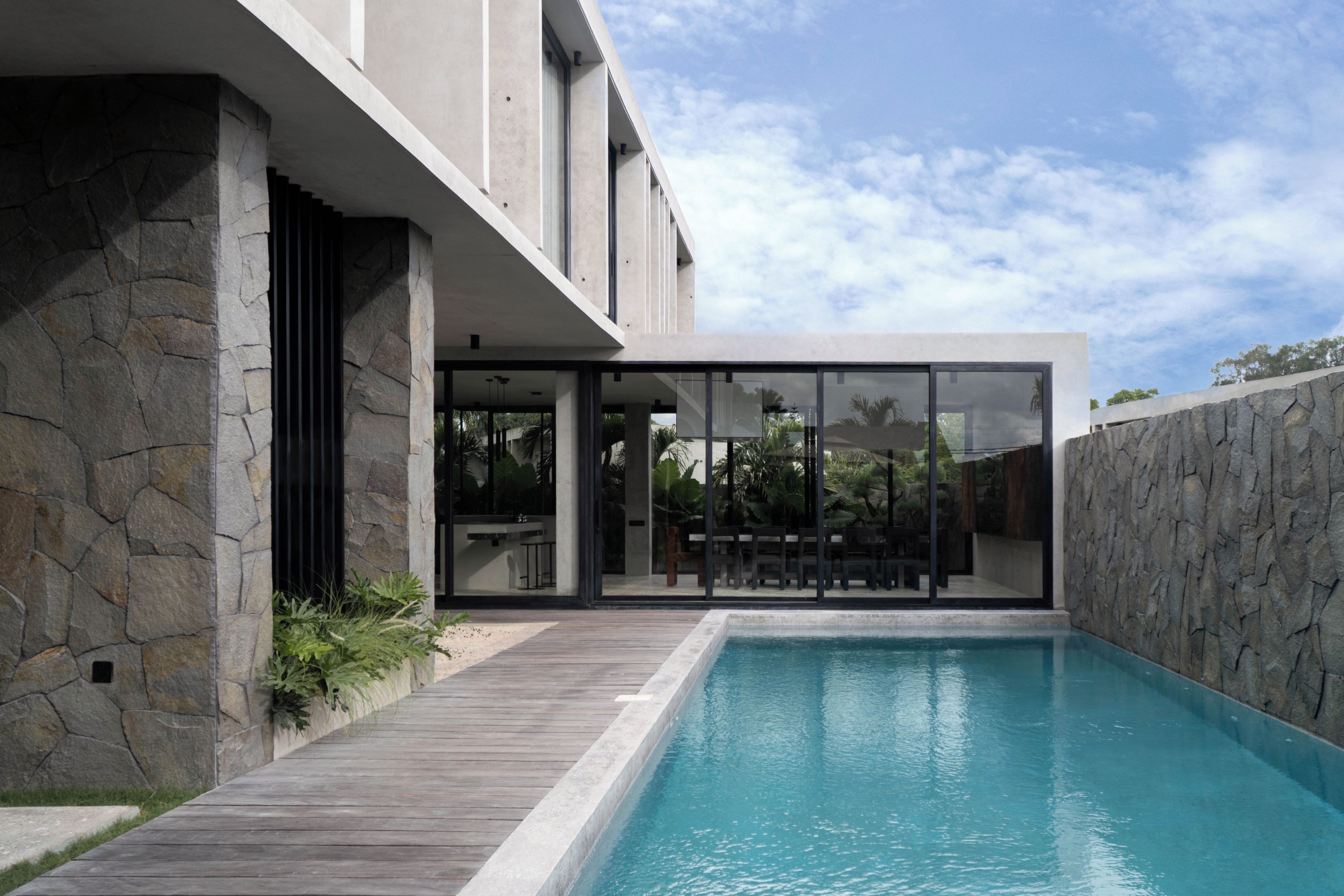 A modern house with a swimming pool, stone walls, and a wooden deck.