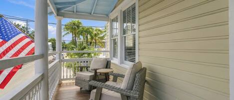 A covered porch with wicker furniture, an American flag, and a view of palm trees.