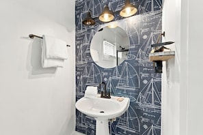 A bathroom with a white sink, a round mirror, and a towel rack. -  Cozy 1-bedroom apartment in old town, offering the perfect island retreat. (Key West)