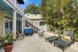 A covered outdoor area with a staircase leading to a second floor, a blue sofa, two lounge chairs with cushions, and a potted plant. -  Cozy 1-bedroom apartment in old town, offering the perfect island retreat. (Key West)