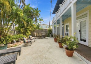 A covered outdoor patio with a dining table and chairs, surrounded by potted plants and palm trees. -  Cozy 1-bedroom apartment in old town, offering the perfect island retreat. (Key West)