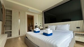 A hotel room with a large bed, a wardrobe, a bathroom, and a TV. - Modern 2 Bed, 2 Bath in Bang Tao - Brand New 75sqm at Ozone (Choeng Thale)