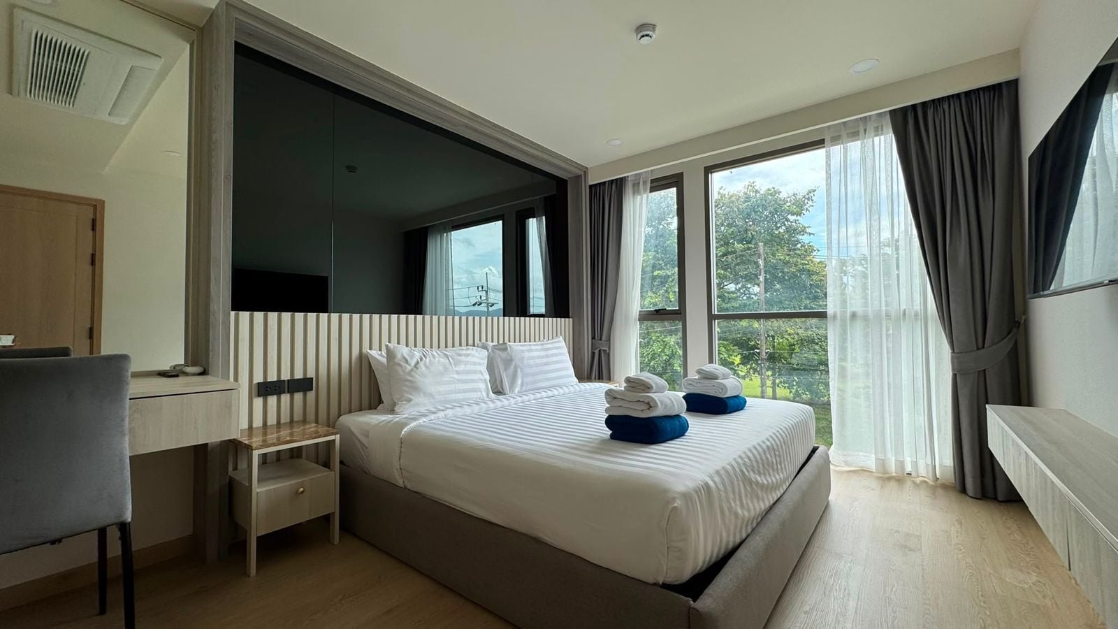 A modern hotel room with a large bed, a desk, and a view of the outdoors.