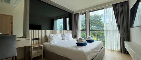 A modern hotel room with a large bed, a desk, and a view of the outdoors.