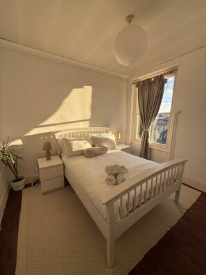 A bedroom with a single bed, bedside tables, a nightstand, a lamp, a potted plant, and a window with curtains. - Sunny 2-bed Triplex With Private Terrace (London)