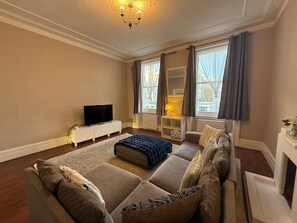 A living room with a large sectional sofa, a television, and a fireplace. - Sunny 2-bed Triplex With Private Terrace (London)