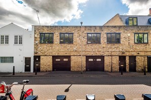 A building with a brick facade, multiple garage doors, and a bicycle parked in front. - Elegant 2-bed Duplex 2 En-suites Belsize Park (London)