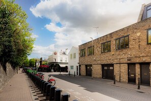 A street view with a row of parked bicycles, a white building with a sign, and a brick building with multiple windows. - Elegant 2-bed Duplex 2 En-suites Belsize Park (London)