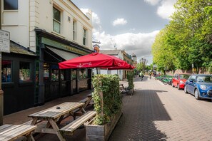 A street with outdoor seating, a red umbrella, and parked cars. - Elegant 2-bed Duplex 2 En-suites Belsize Park (London)