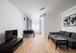A modern living room with a flat-screen TV, a sofa, a coffee table, and a dining area with chairs and a table. - Praga Południe Harmony Apartment (Warszawa)