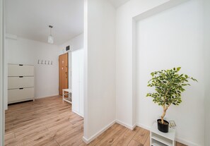 A hallway with a wooden floor, white walls, a door with a coat of arms, and a potted plant. - Praga Południe Harmony Apartment (Warszawa)