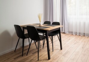 A dining table with four chairs, a vase with dried plants, and sheer curtains. - Praga Południe Harmony Apartment (Warszawa)