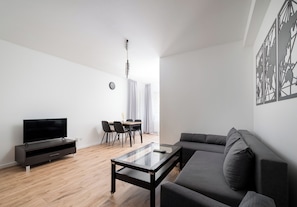 Una sala moderna con un televisor de pantalla plana, una mesa de centro de vidrio, un sofá gris y un comedor con mesa y sillas.