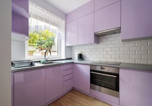 Una cocina con armarios morados, una campana extractora de acero inoxidable y un ventanal con vistas a zonas verdes.