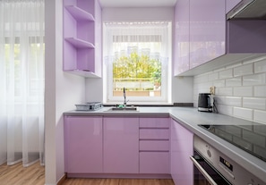 Een moderne keuken met paarse kastjes, een raam met uitzicht op bomen en een zwarte koffiemachine op het aanrecht.