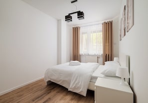 Une chambre à coucher au style minimaliste, avec un lit, une table de chevet et une fenêtre avec des rideaux.