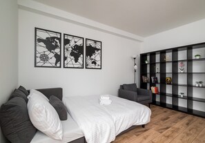 A modern bedroom with a bed, a grey armchair, a bookshelf, and a world map artwork on the wall. - Praga Południe Harmony Apartment (Warszawa)