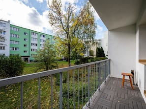 Un balcone con uno sgabello di legno, una ringhiera e vista su un edificio verde e alberi.