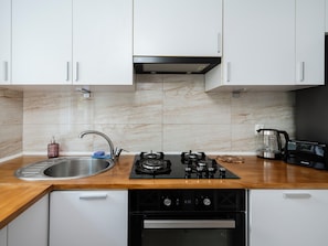 Una cucina moderna con mobili bianchi, un lavello in acciaio inossidabile, un piano cottura a gas e una macchina da caffè.