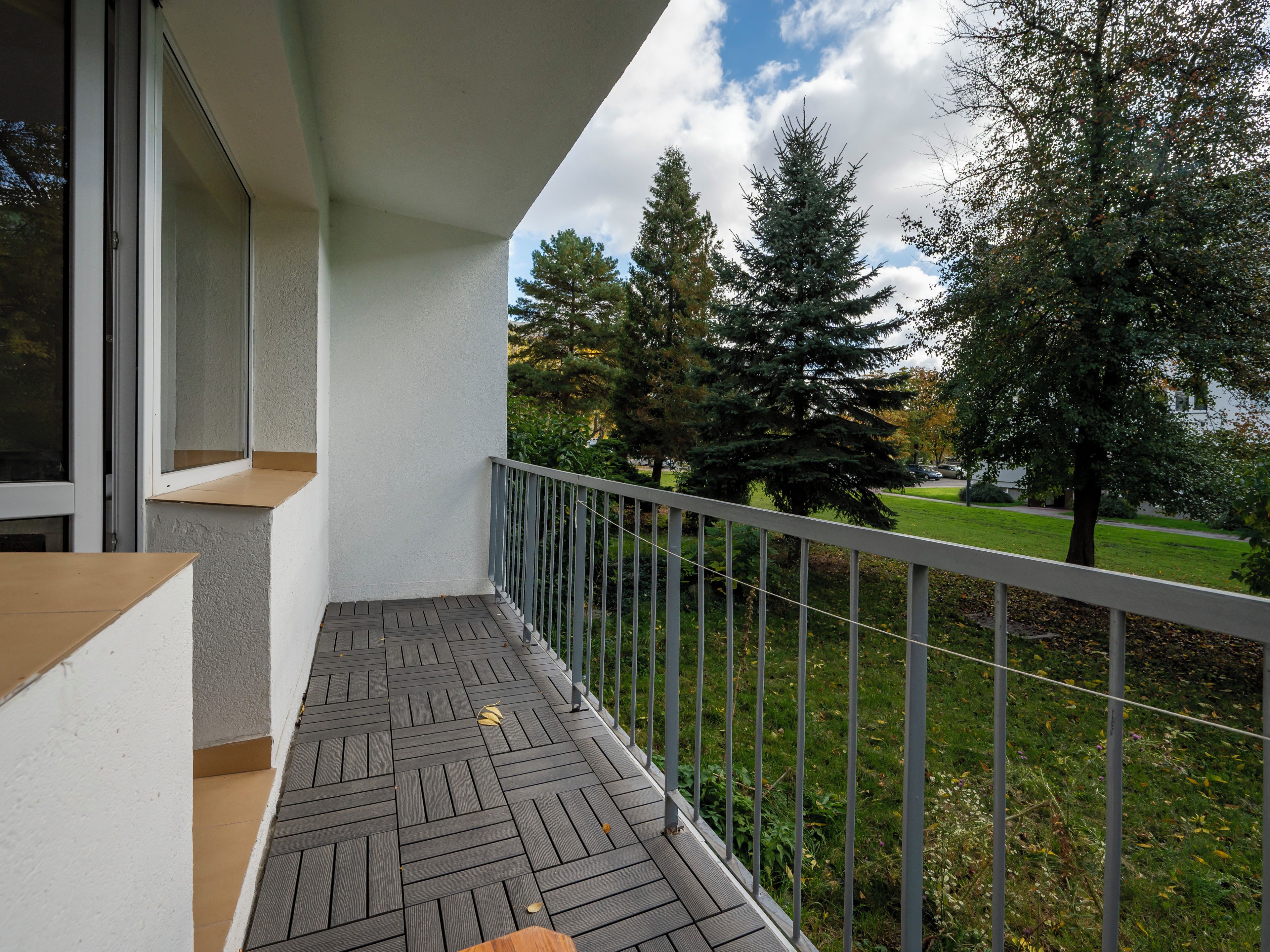 Un balcon doté d’un plancher en bois, d’une rambarde en métal et offrant une vue sur les arbres et l’herbe.