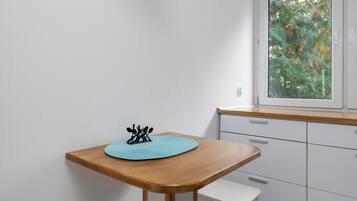 Una cocina pequeña con una mesa de madera, un tapete azul y una ventana con vistas a árboles.