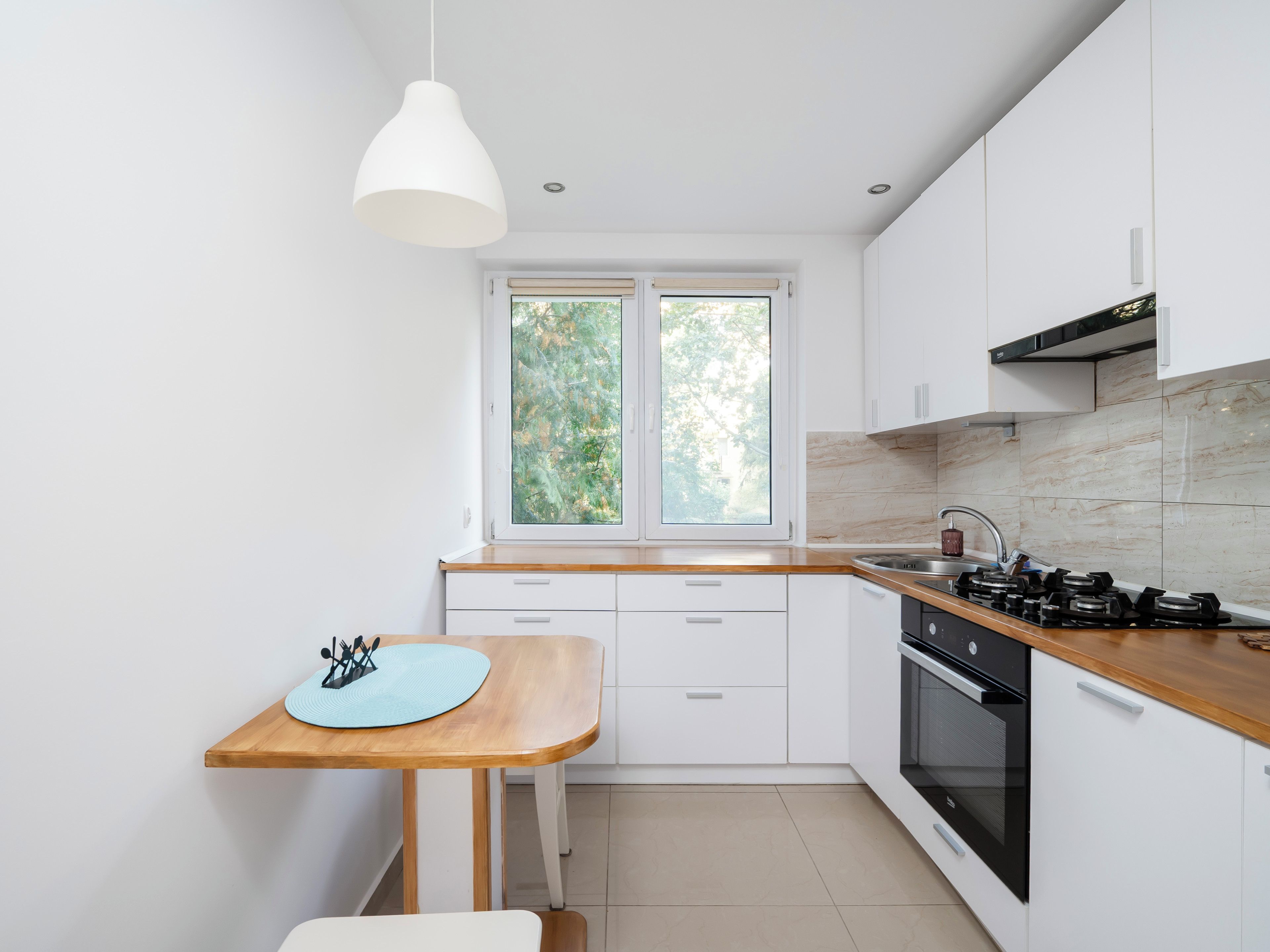 Une cuisine moderne avec des armoires blanches, un plan de travail en bois, un four encastré et une fenêtre donnant sur un paysage verdoyant.